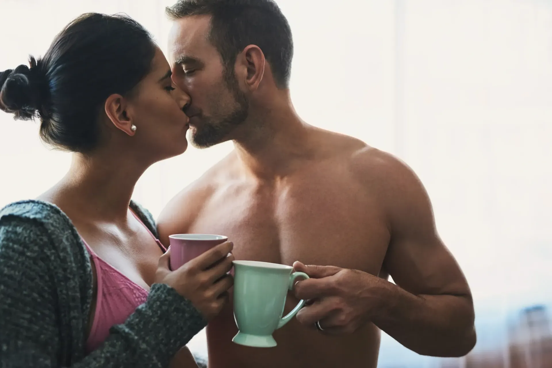 A man and a woman are kissing while holding cups of coffee.