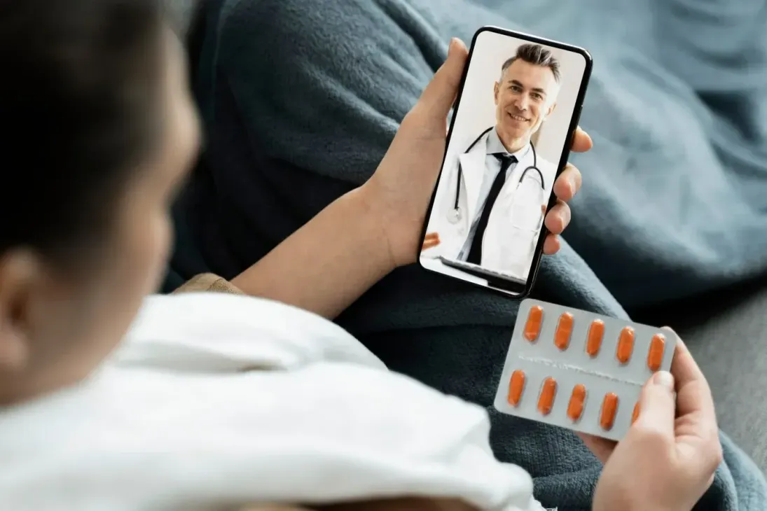 A woman is holding a blister of pills and talking to a doctor on her phone.