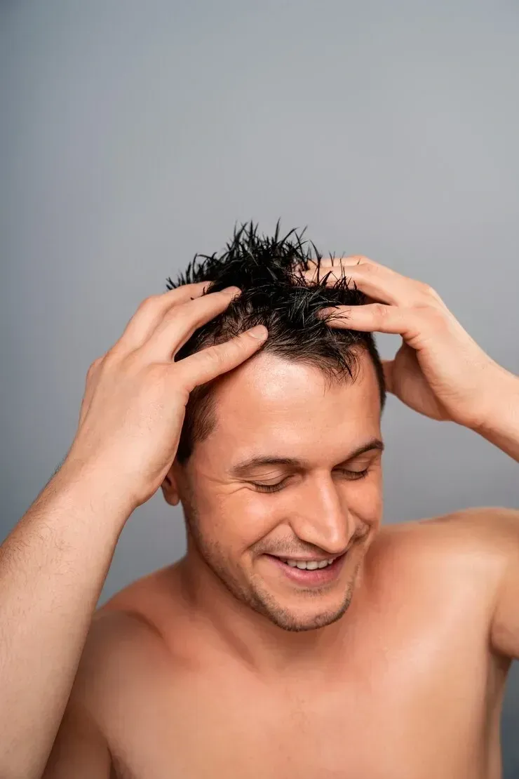 A shirtless man is washing his hair with his hands.