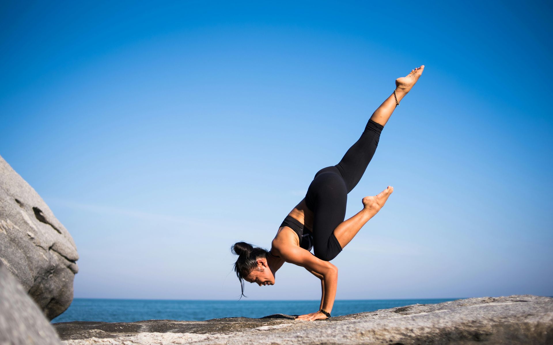 A woman is doing a handstand on a rock near the ocean.