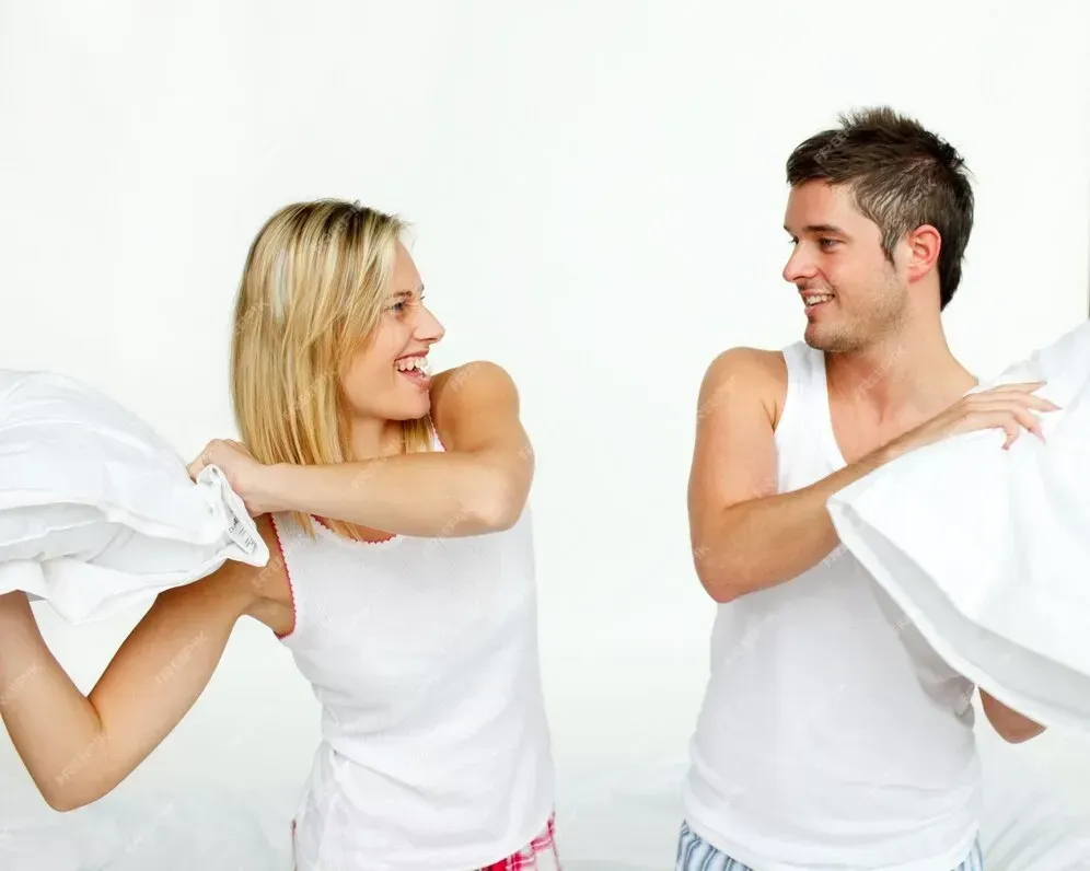 A man and a woman are having a pillow fight on a bed.