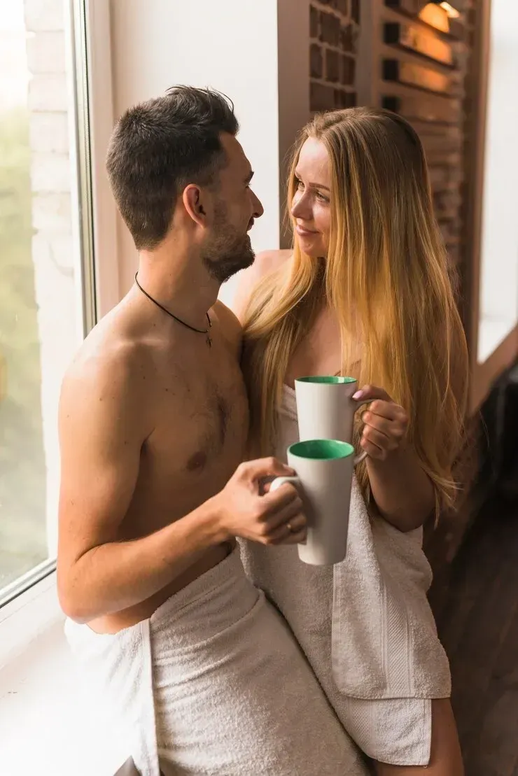 A man and a woman are wrapped in towels and holding cups of coffee.