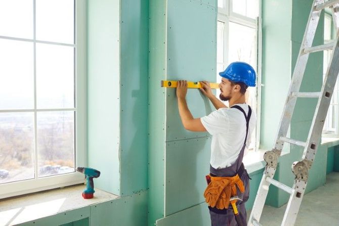 Construction worker using a level on a drywall wall by a window.