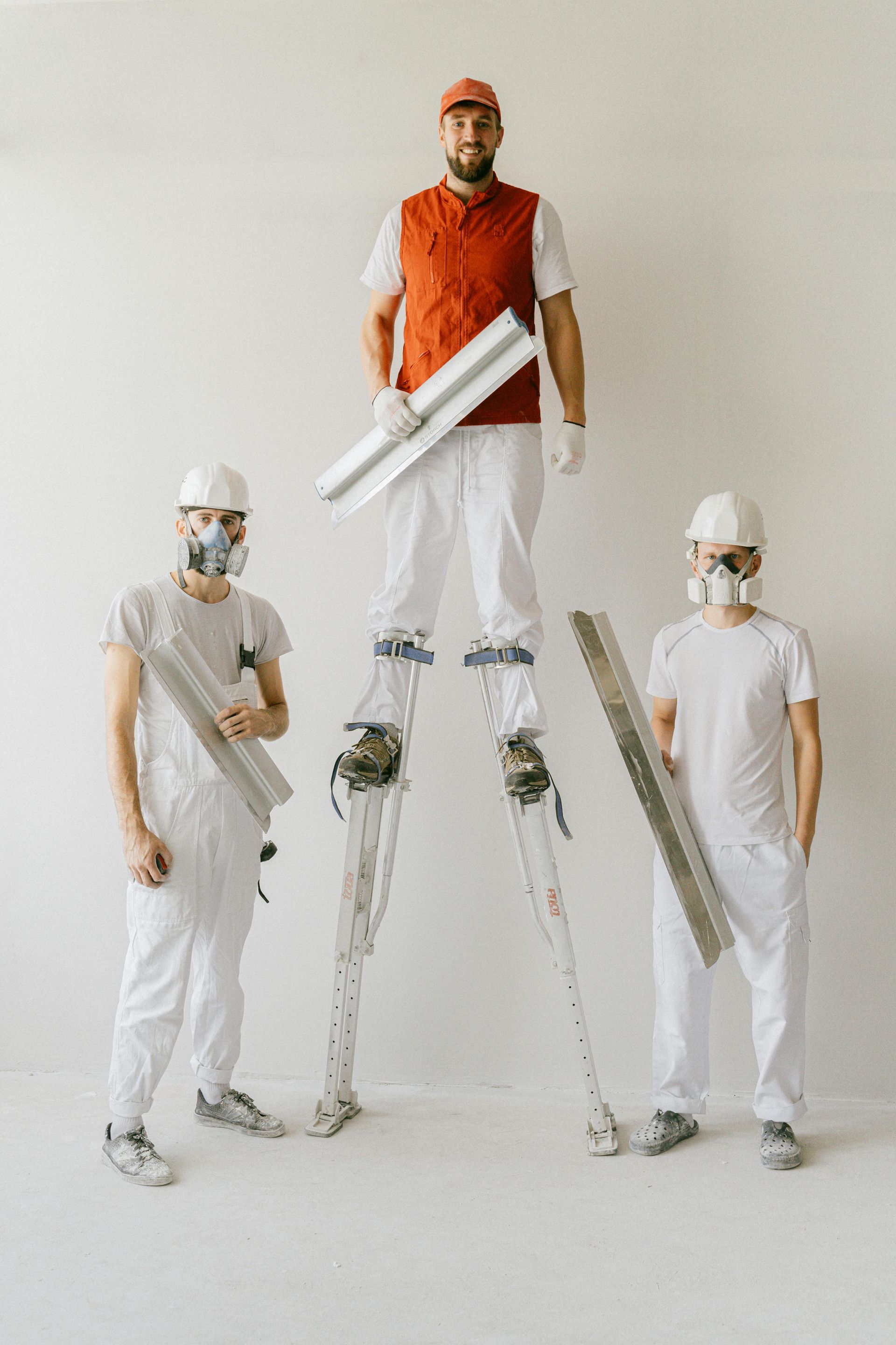 Three people holding plastering tools against a white wall.