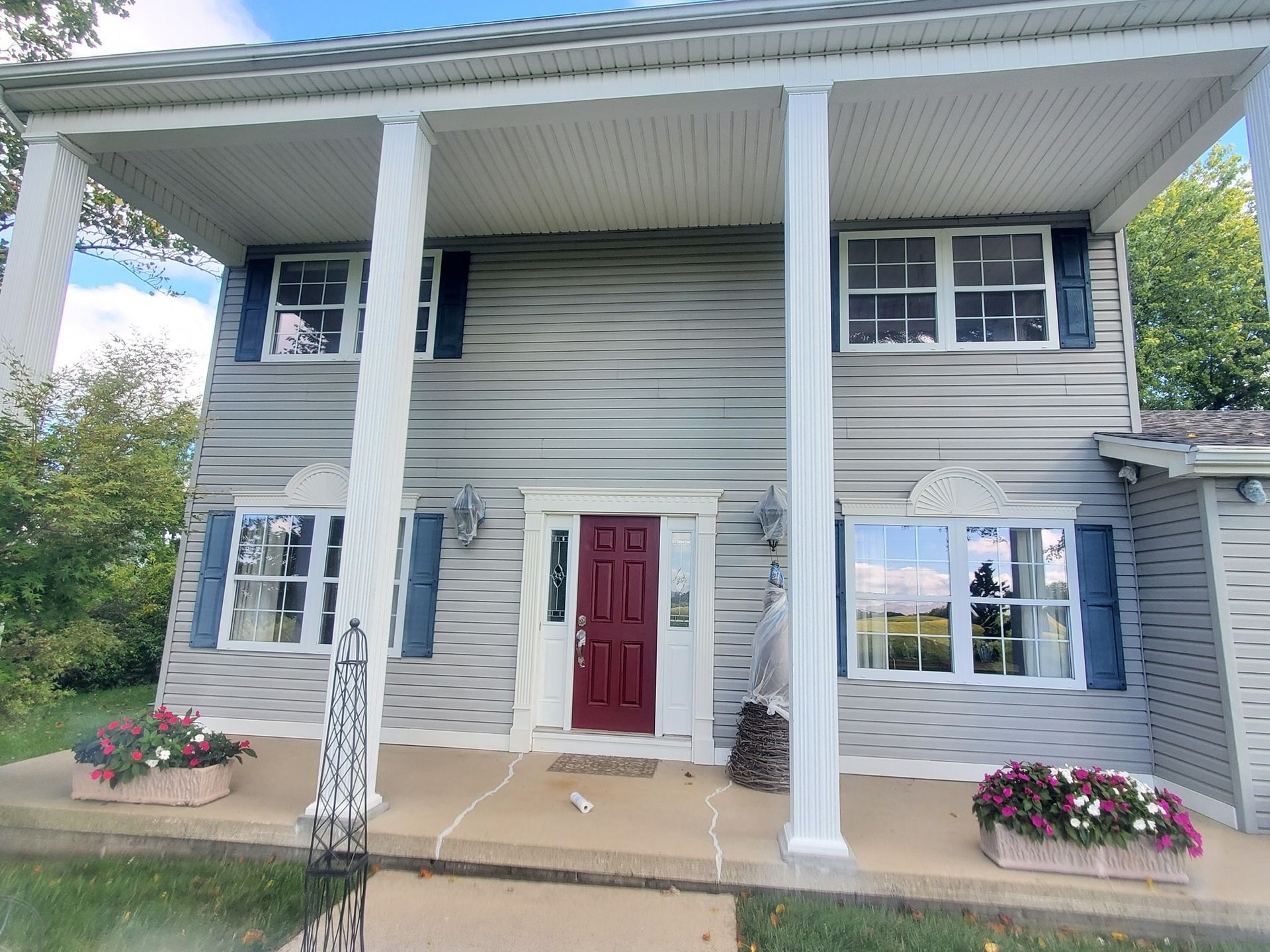 A two-story grey house with white columns, a red front door, blue shutters, and flower boxes on the front porch.
