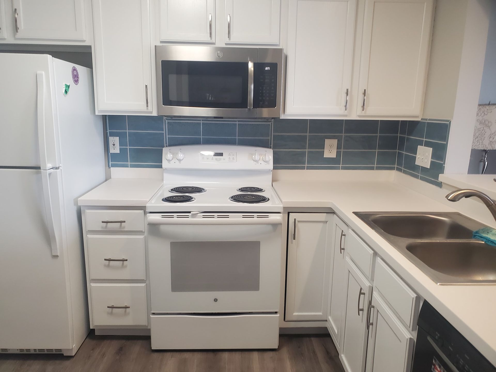 A bright kitchen with white cabinets, white appliances, a blue subway tile backsplash, and a double-basin stainless sink.