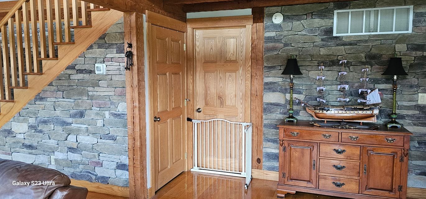 A wooden staircase leads up beside a natural stone wall, two wooden doors, and a sideboard displaying a model ship.