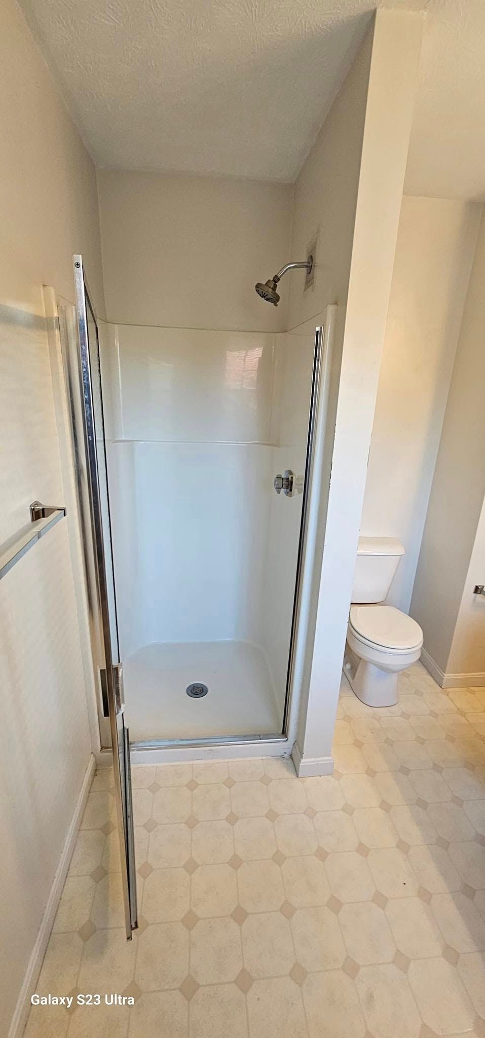 A bathroom featuring a glass-enclosed shower stall with a white base next to a white toilet on a patterned tiled floor.