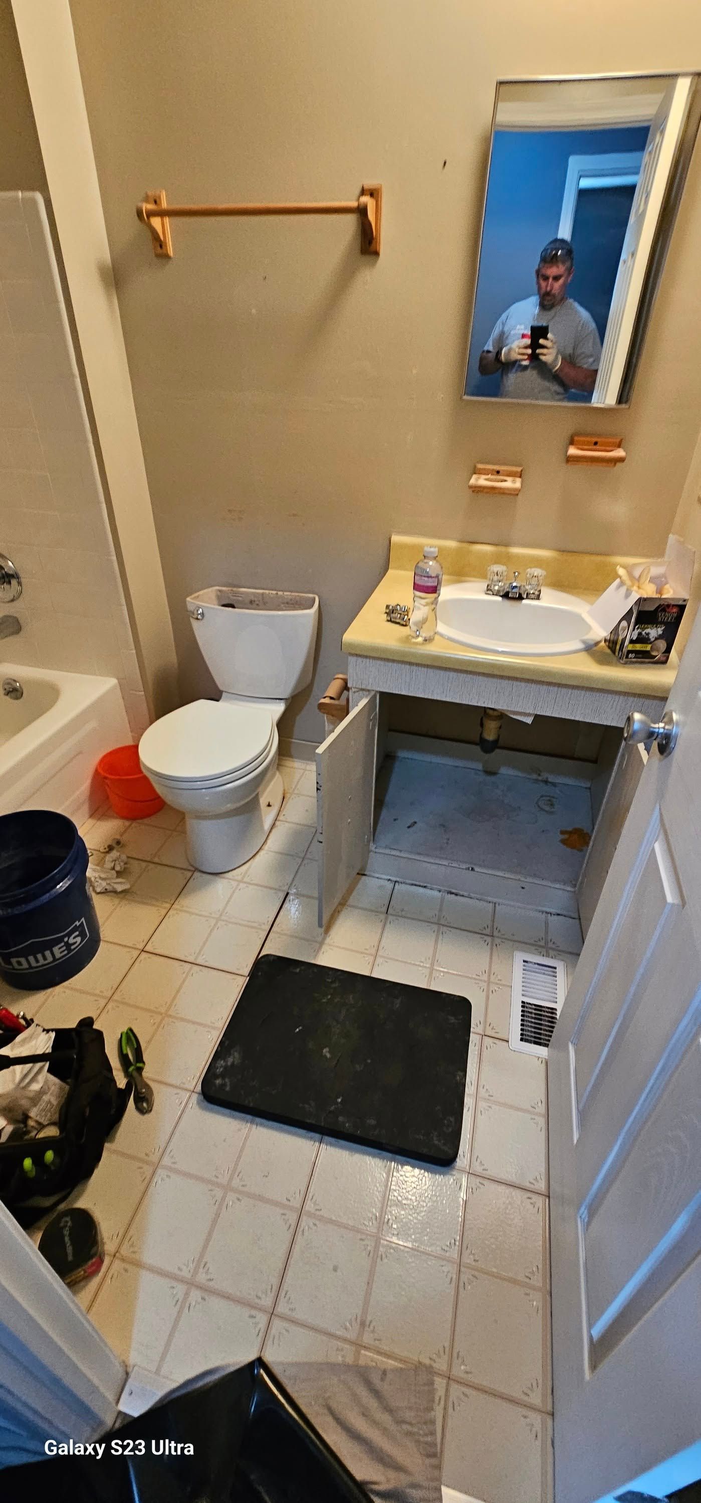 A cluttered bathroom featuring a white toilet, a vanity with a yellow countertop, a mirror, and tiled floors.