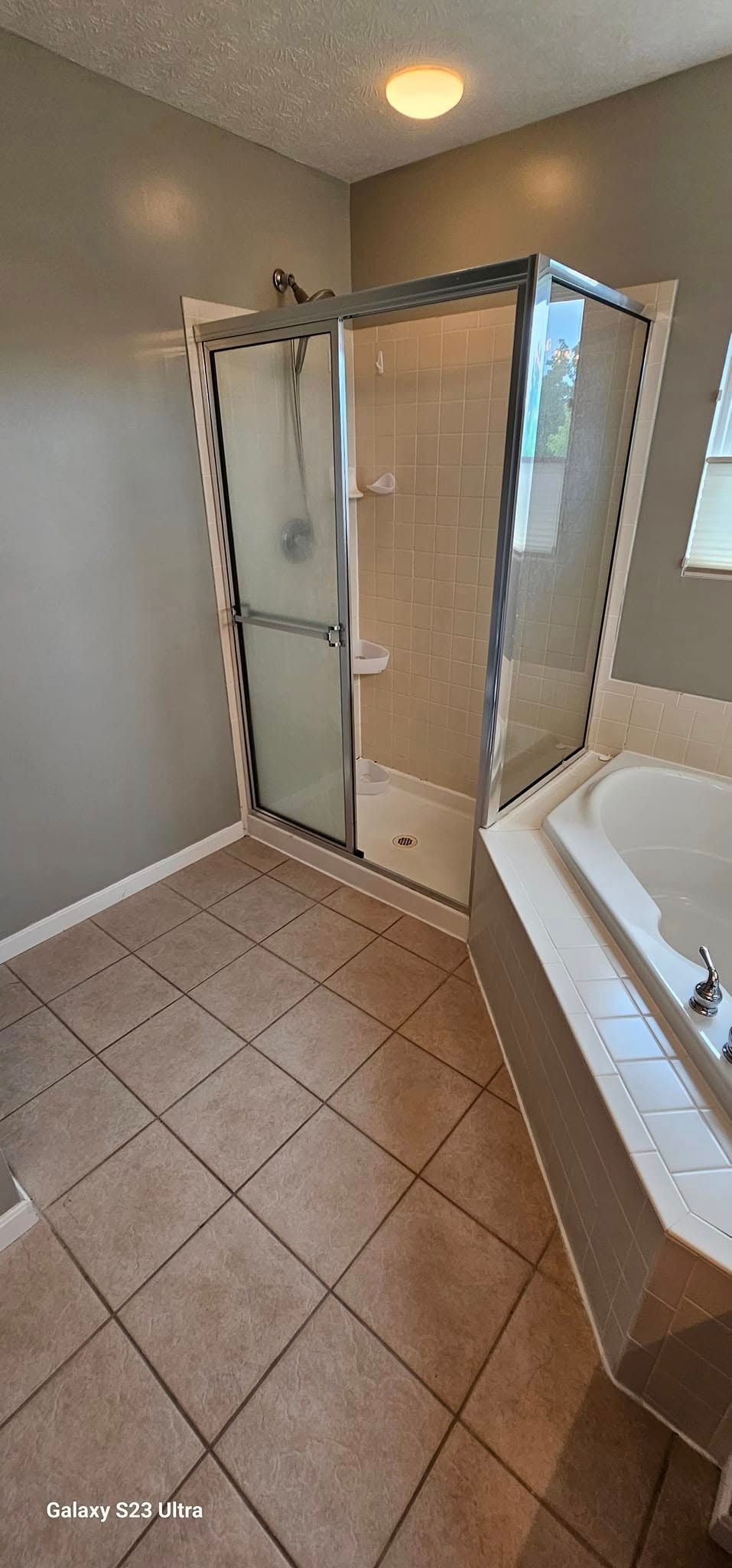 A walk-in shower with a silver frame and glass door beside a large corner bathtub in a tiled bathroom.