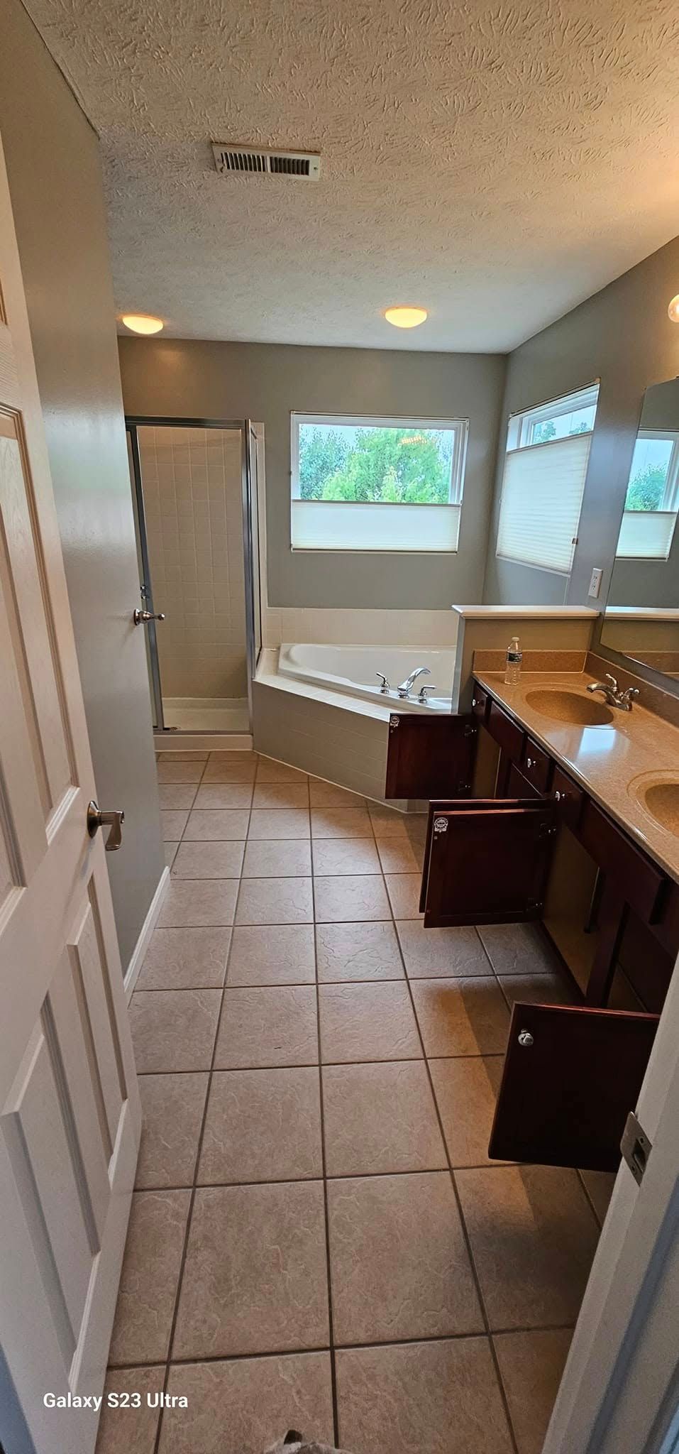 A bathroom with tile floors, a corner soaking tub, a walk-in shower, and a double vanity under a wide mirror.