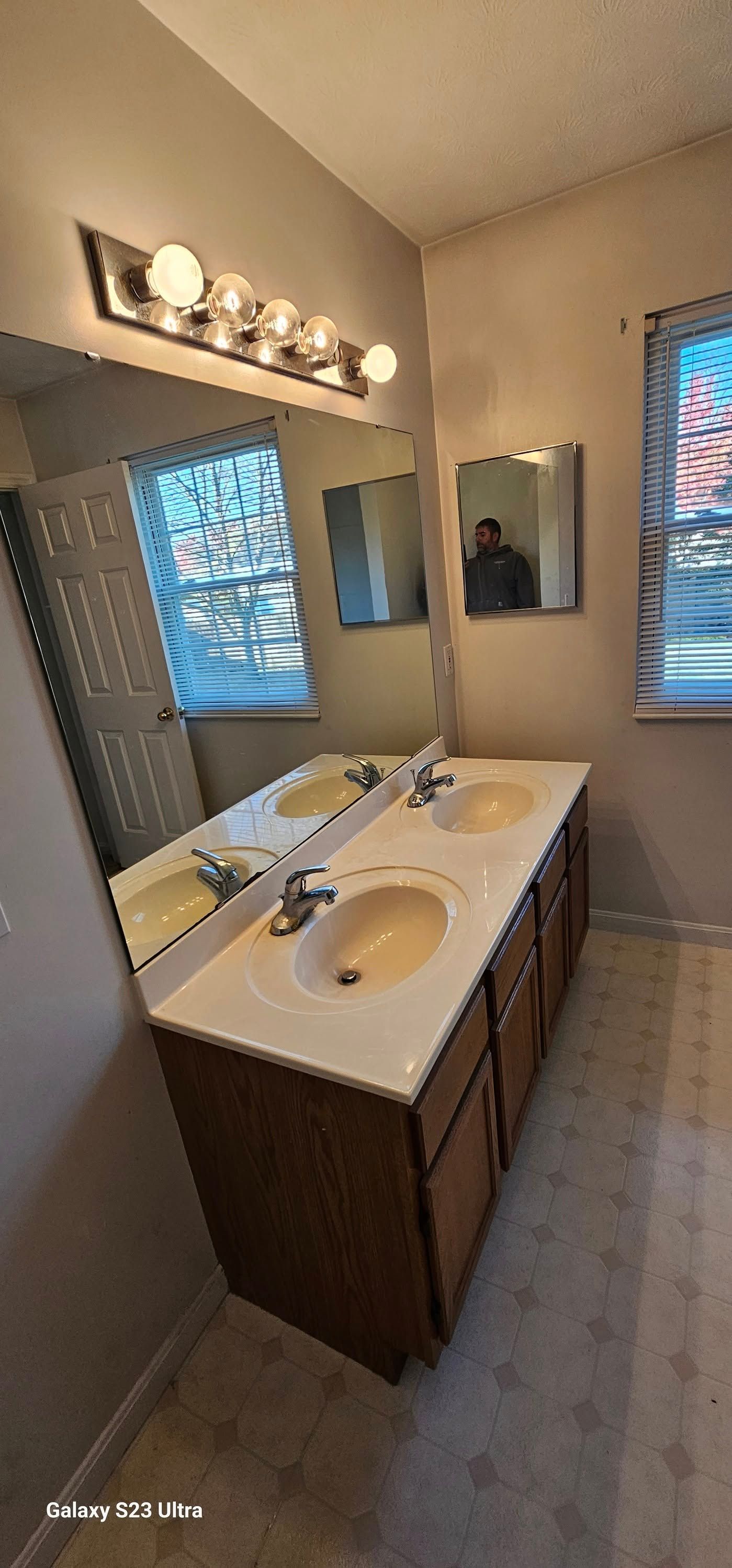 Bathroom vanity with a double-sink white countertop, wood cabinetry, a large mirror, and a five-bulb light fixture.