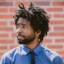 A man with dreadlocks and a beard wearing a blue shirt and tie