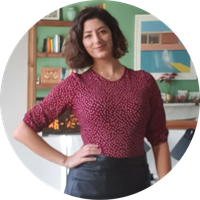 A woman in a maroon top and black skirt stands with her hand on her hip