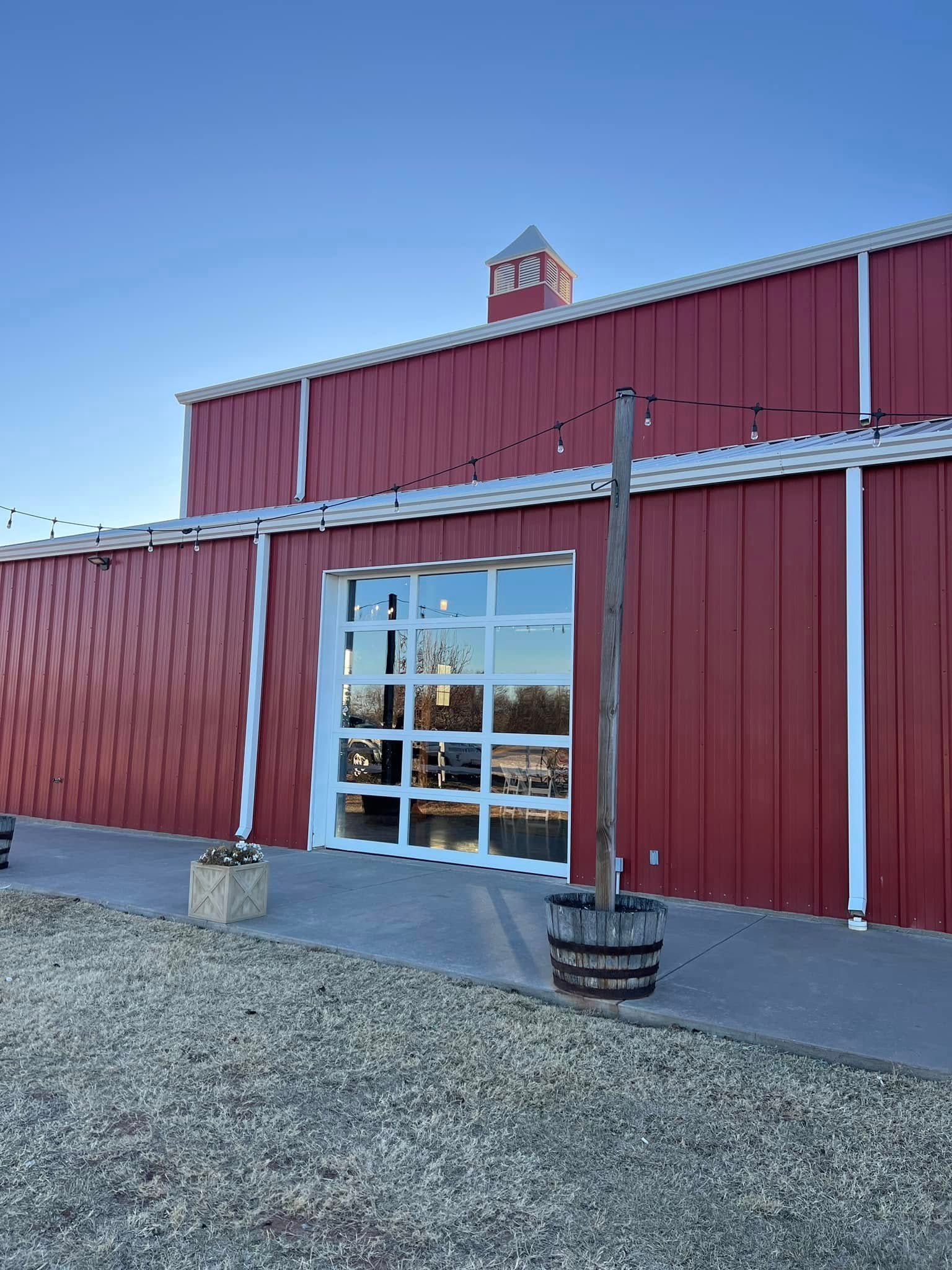 Red barn with glass door, small cupola, and string lights on a sunny day.