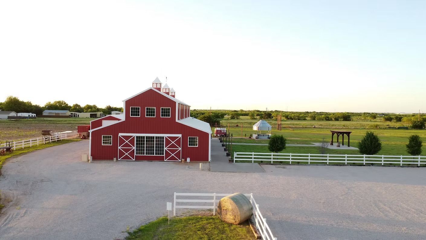 Red barn-like building with white trim and a gravel driveway, in a field, under a clear sky.