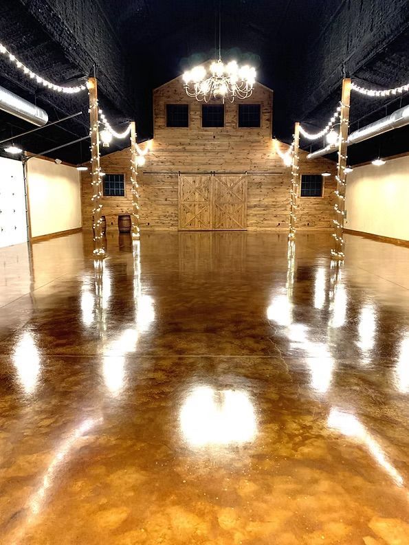 Spacious barn interior with polished brown floor, wooden walls, and decorative lights.