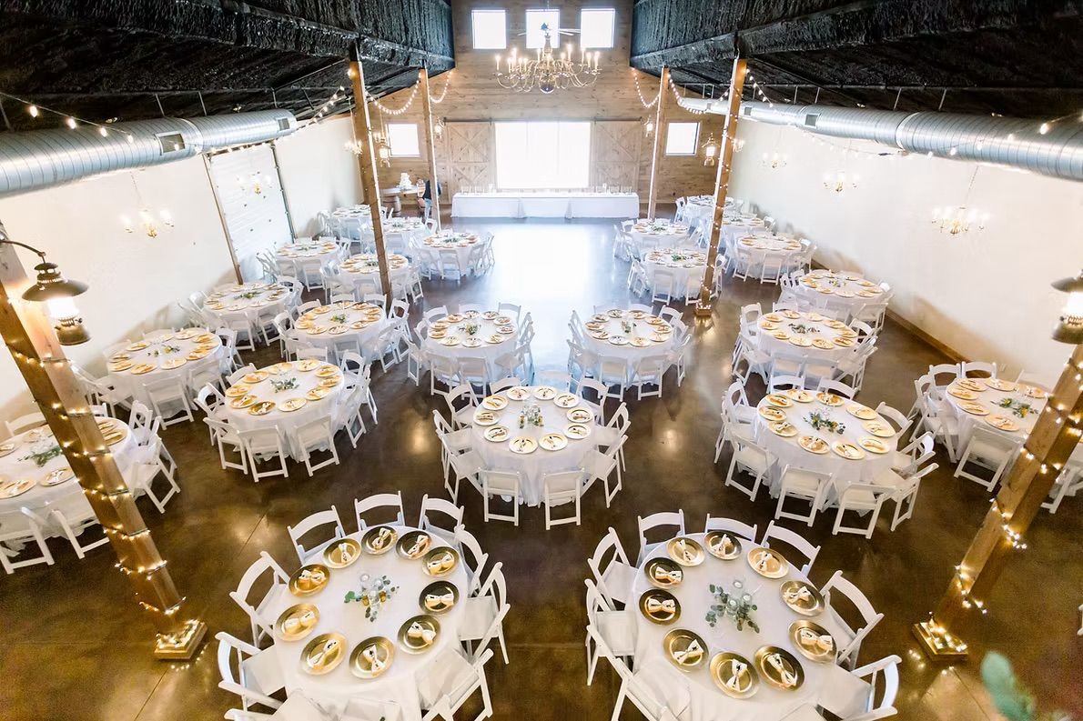 Reception hall set up for a wedding, with round tables, white chairs, and floral centerpieces.