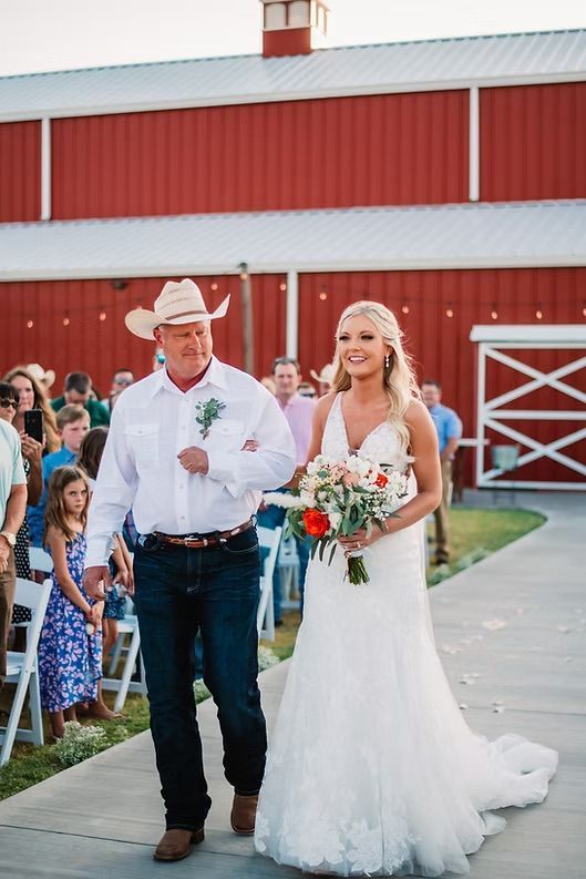 Bride walks down aisle with father, red barn in background.