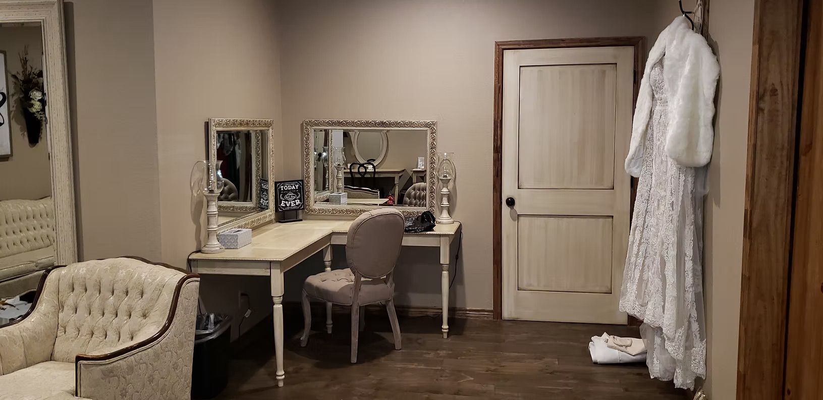 A dressing room with a vanity, chair, and a dress hanging near a door.