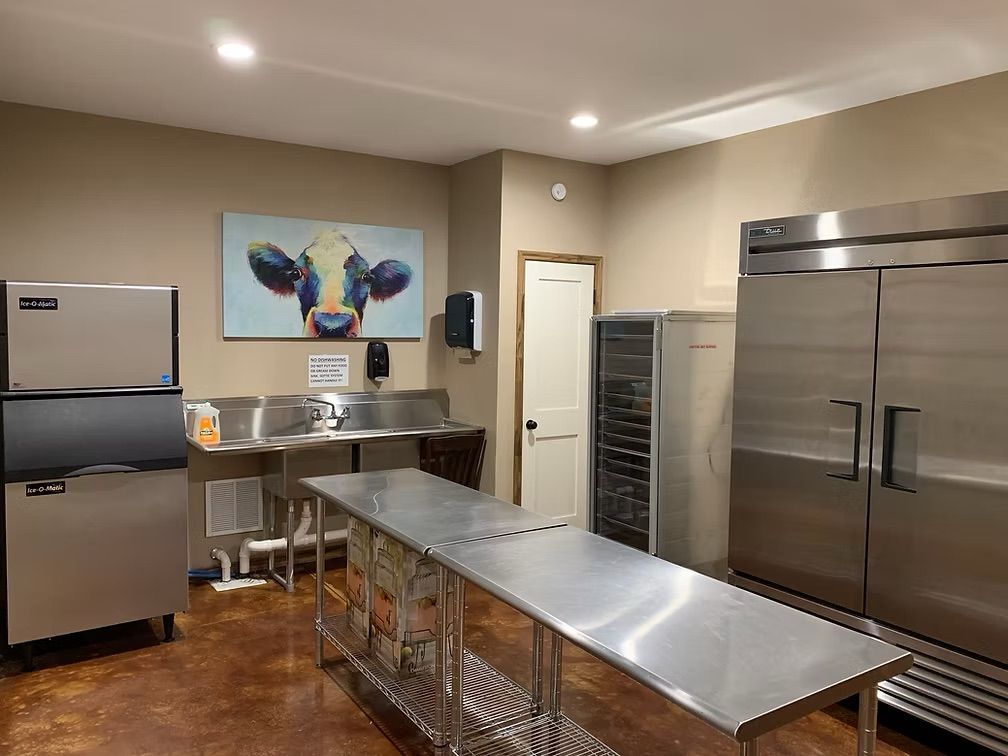 Commercial kitchen with stainless steel appliances, prep table, sinks, and cow art.