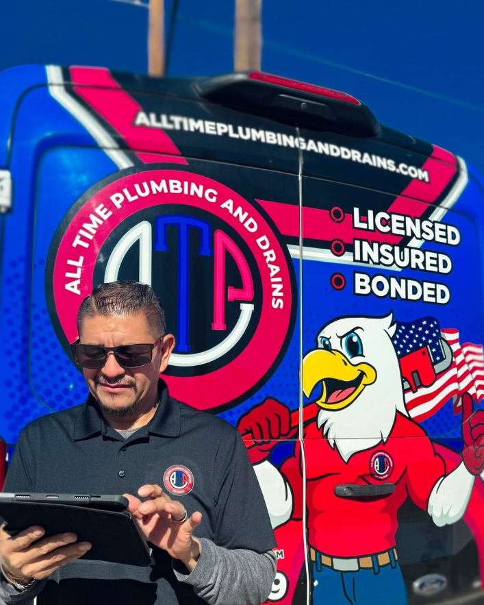 A man is standing in front of an all time plumbing and drains truck