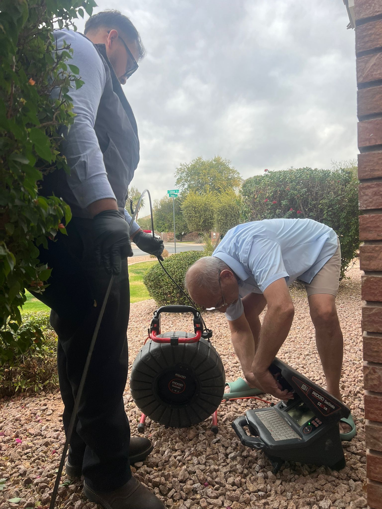 Two men are working on a drain in a yard.