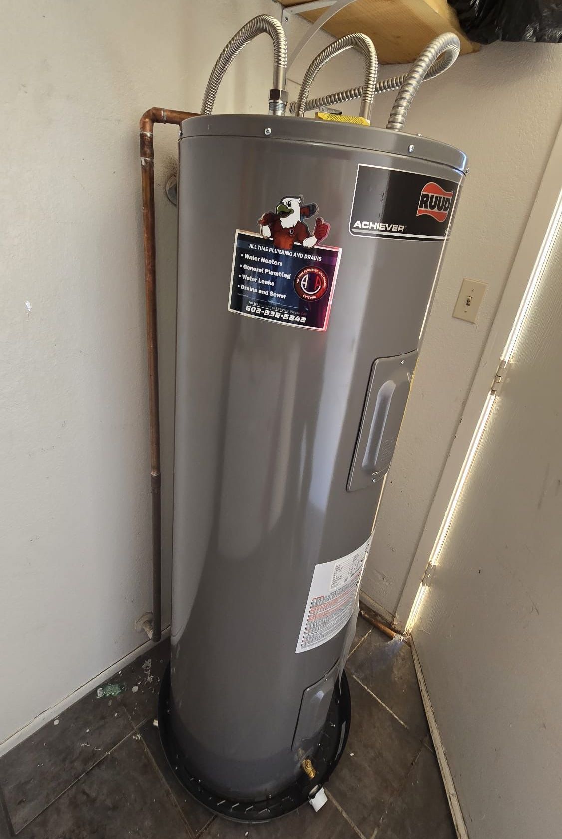 A gray water heater is sitting in a room next to a door.