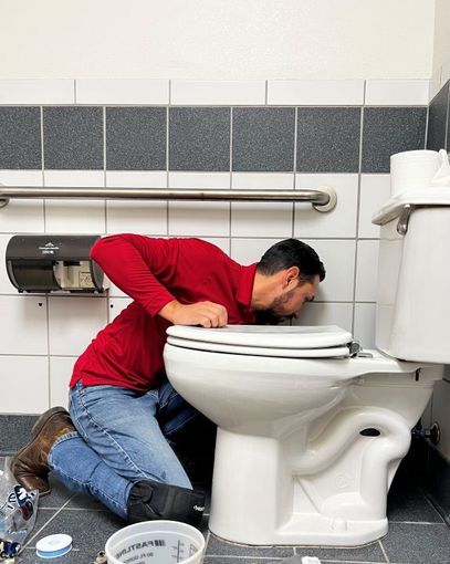 A man in a red shirt is fixing a toilet