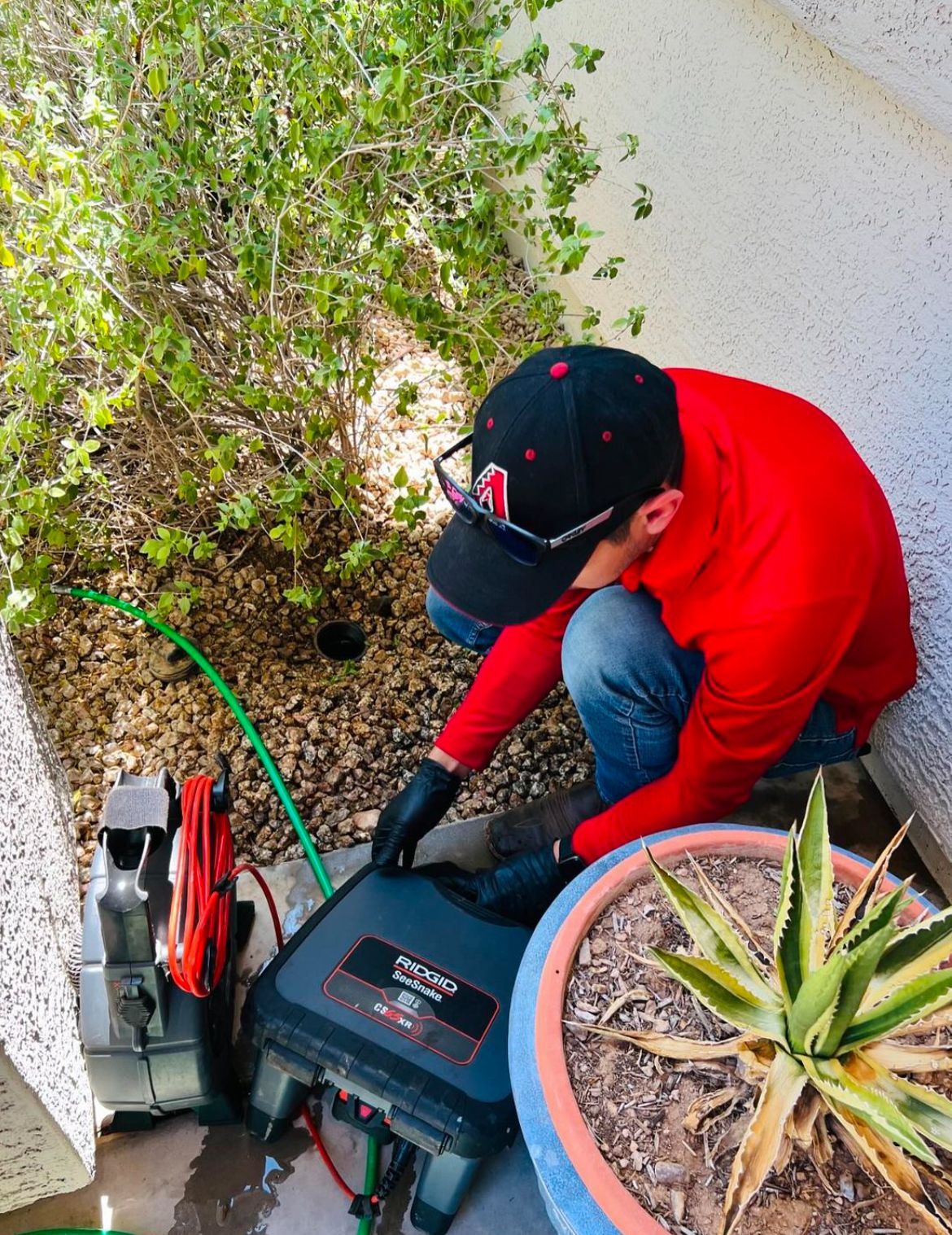 A man in a red shirt and black hat is working on a machine