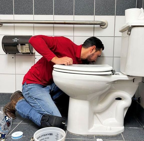 A man in a red shirt is fixing a toilet