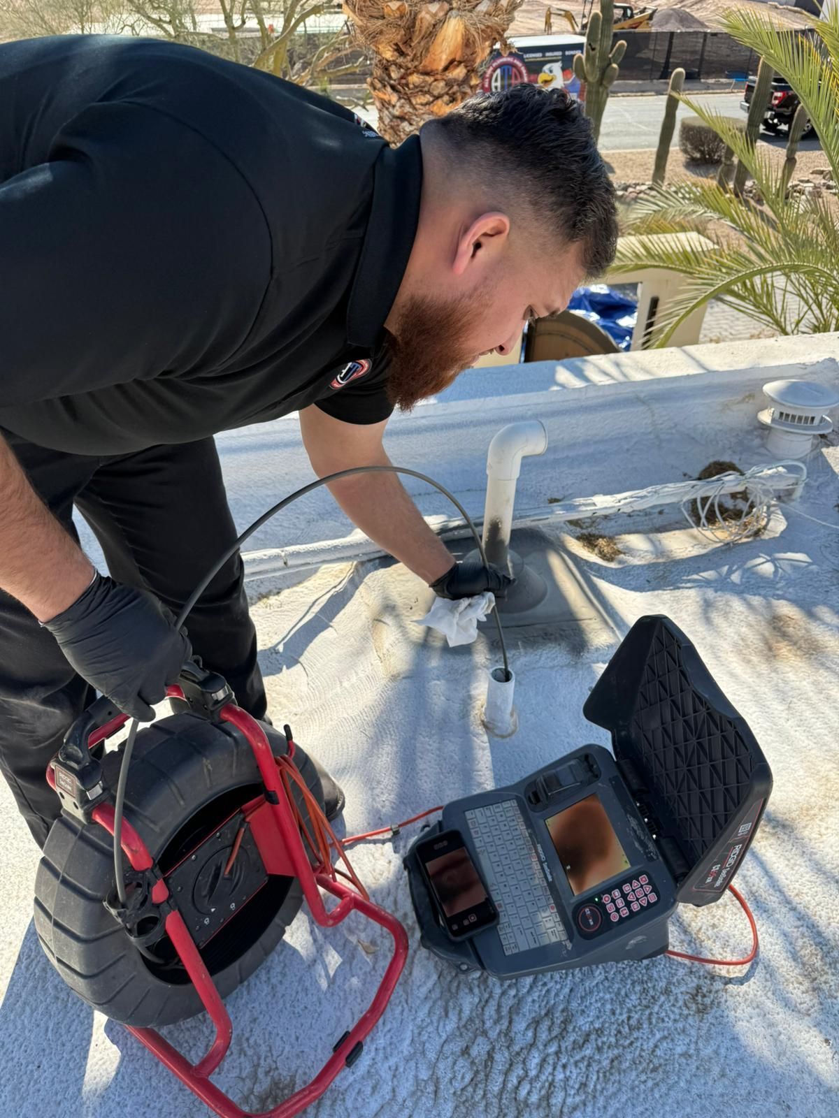 A man is using a camera to look at a pipe on a roof.