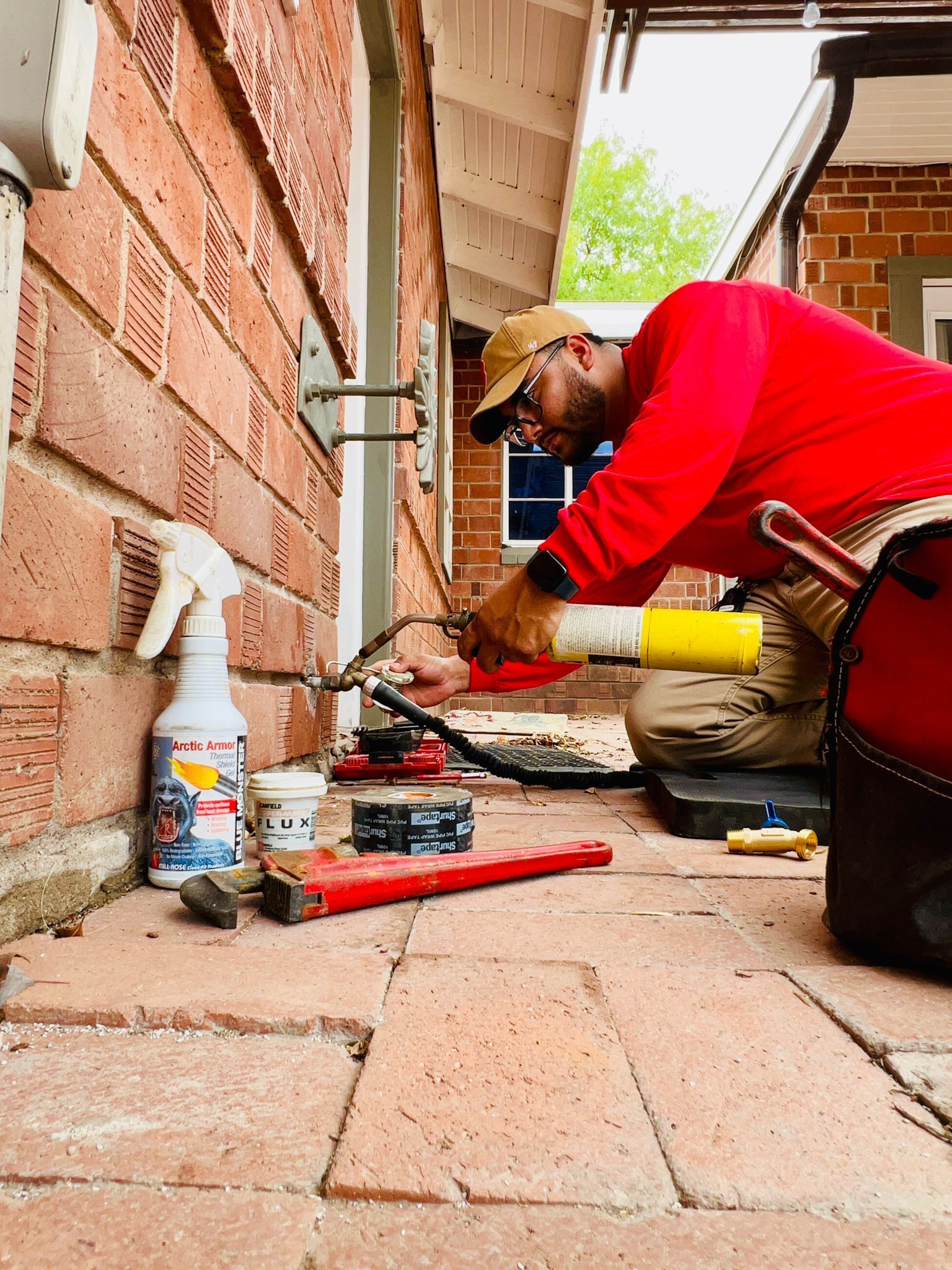 A man is kneeling down on a brick sidewalk working on a pipe.