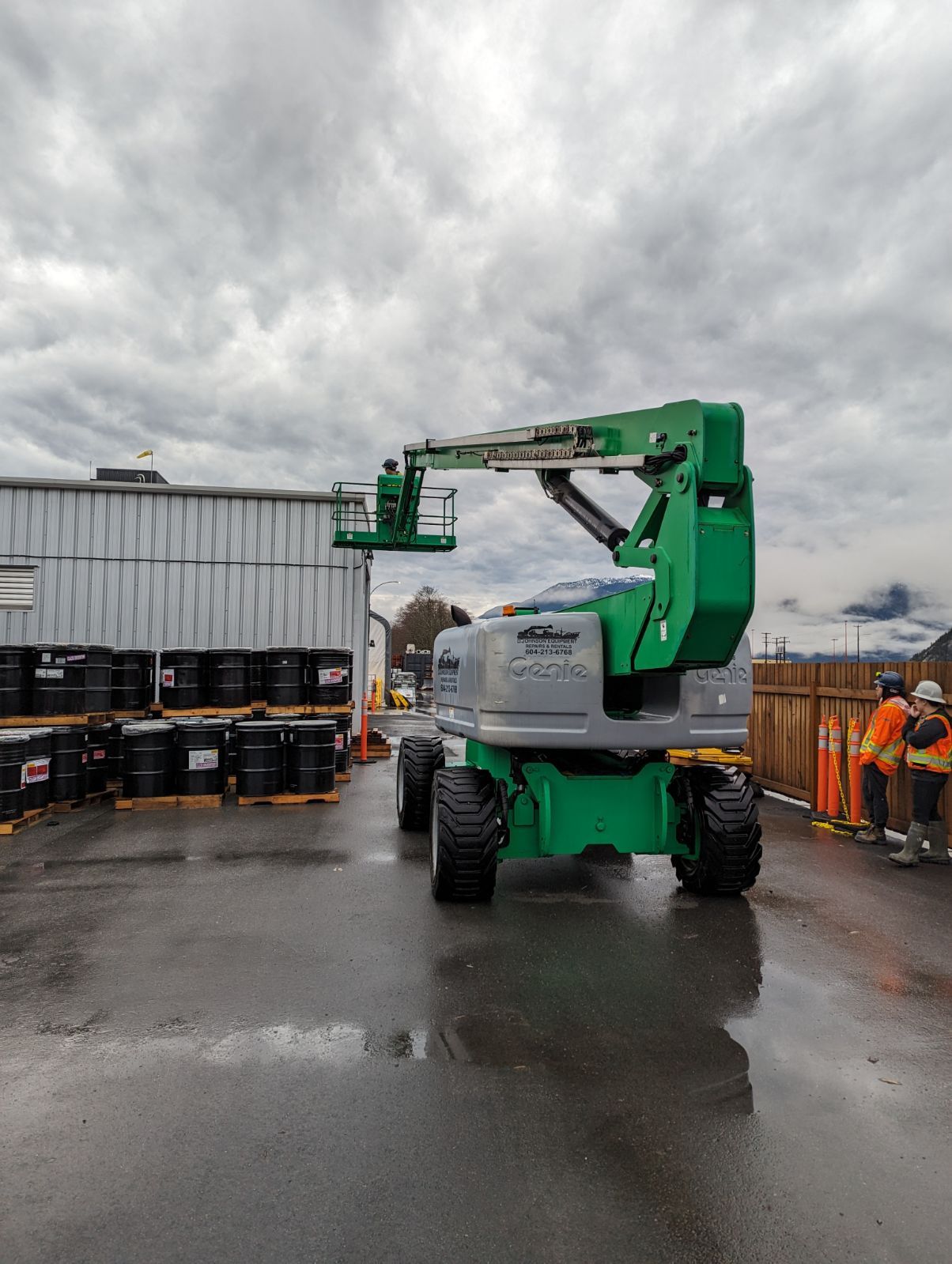 A green aerial lift is parked in front of a building.