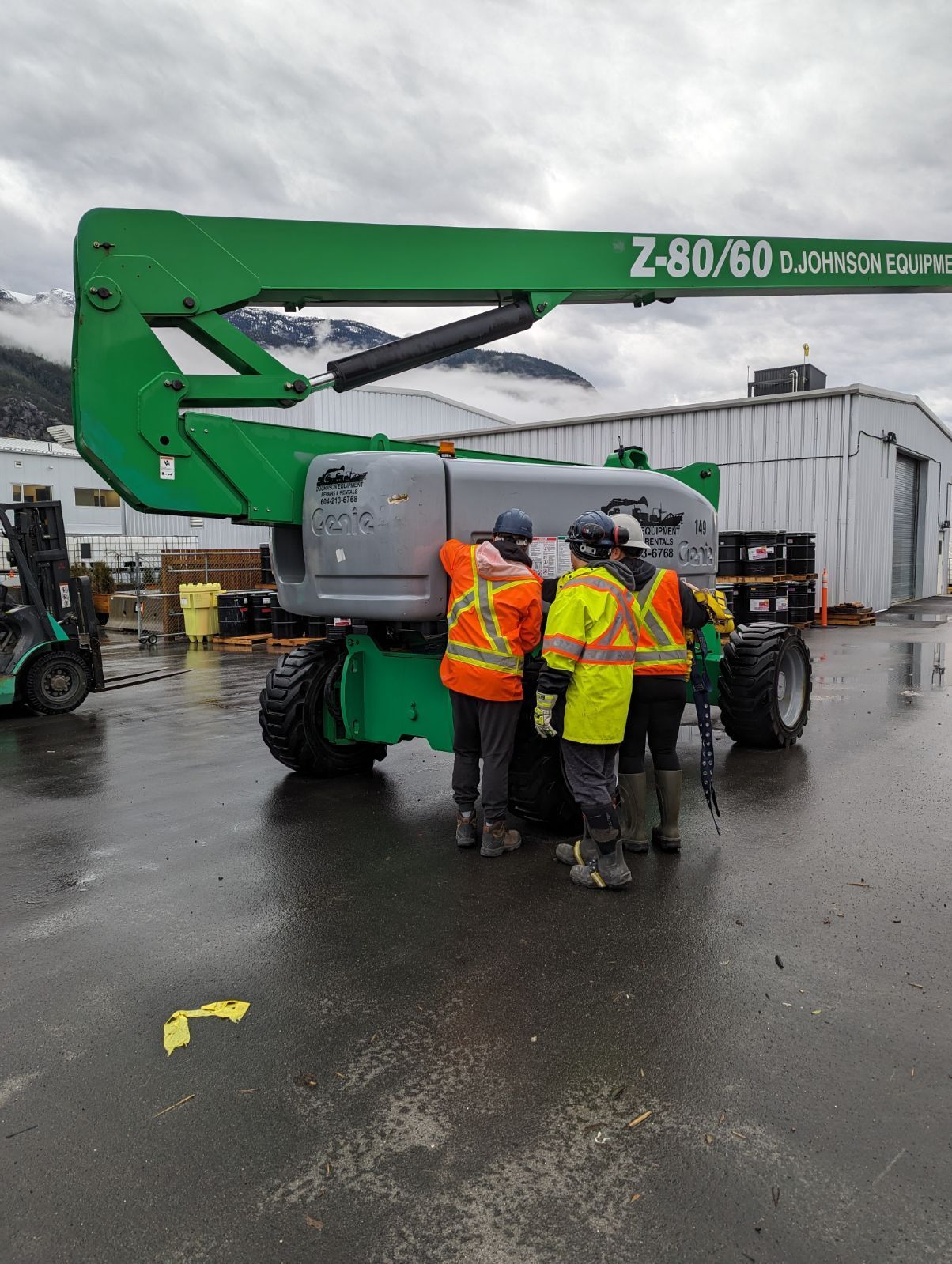 A group of construction workers are standing around a green crane.