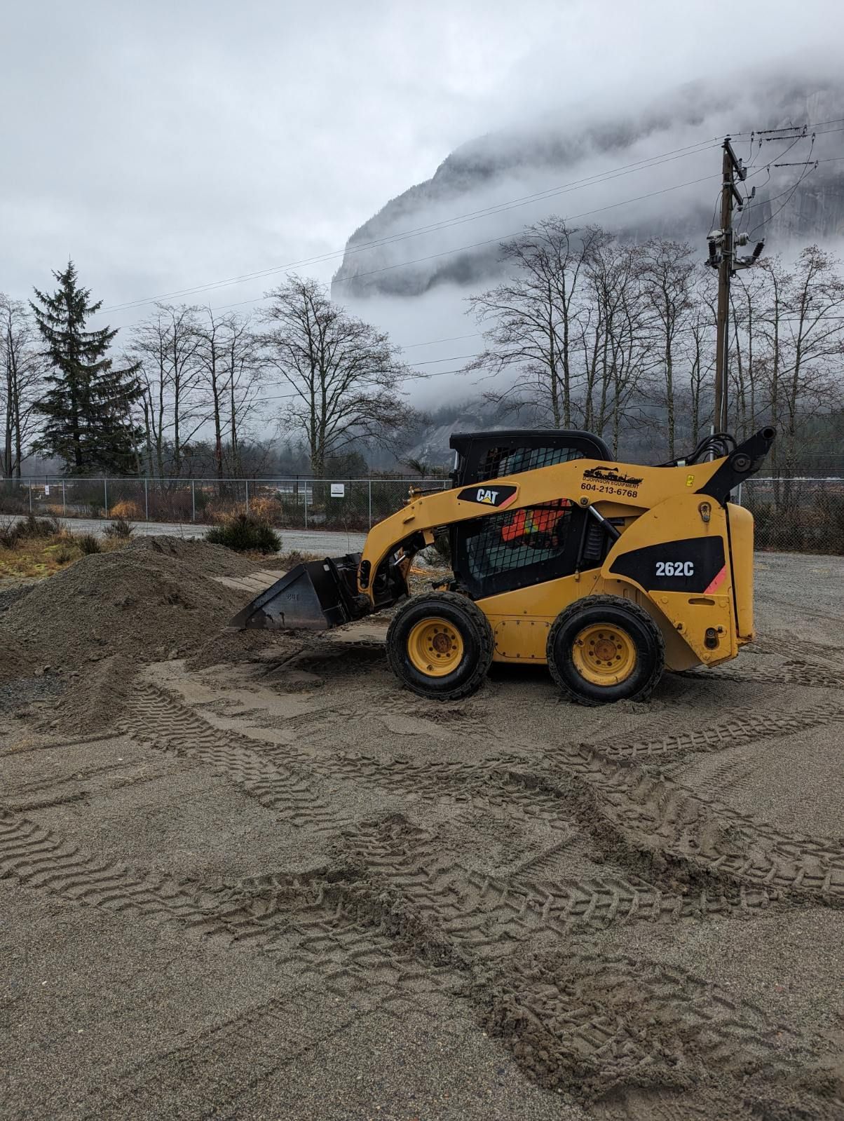 A yellow bulldozer is sitting in a dirt lot with a mountain in the background.