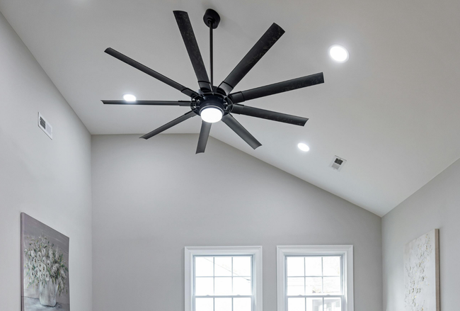 Modern room with vaulted ceiling, black ceiling fan, recessed lights, and two windows above a wall painting