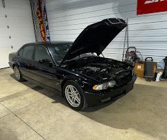A black car with the hood up is parked in a garage.