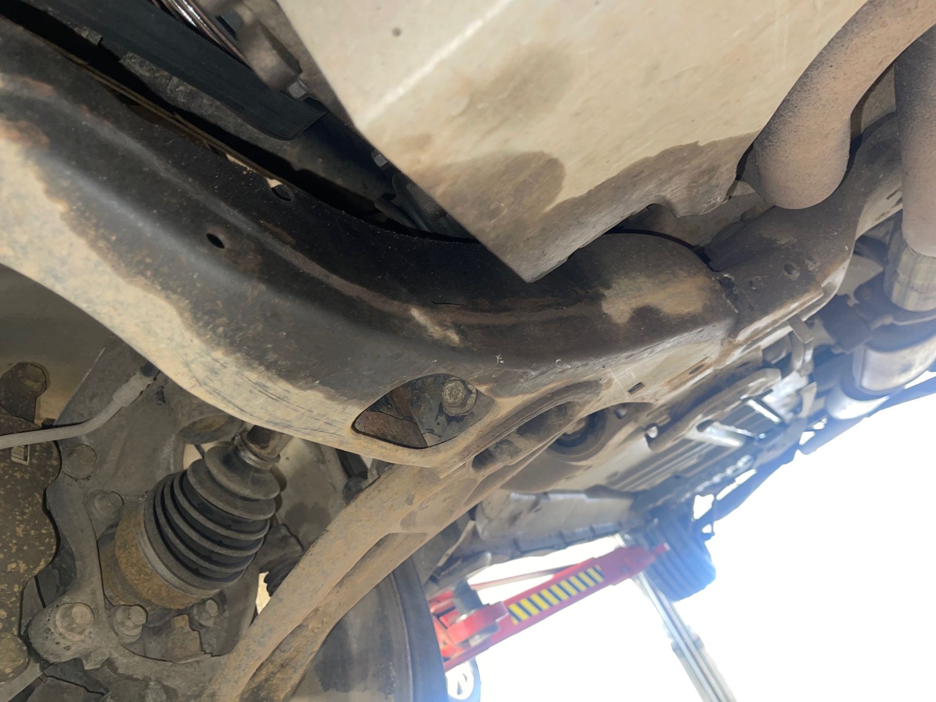 A close up of the underside of a car with a jack in the background.