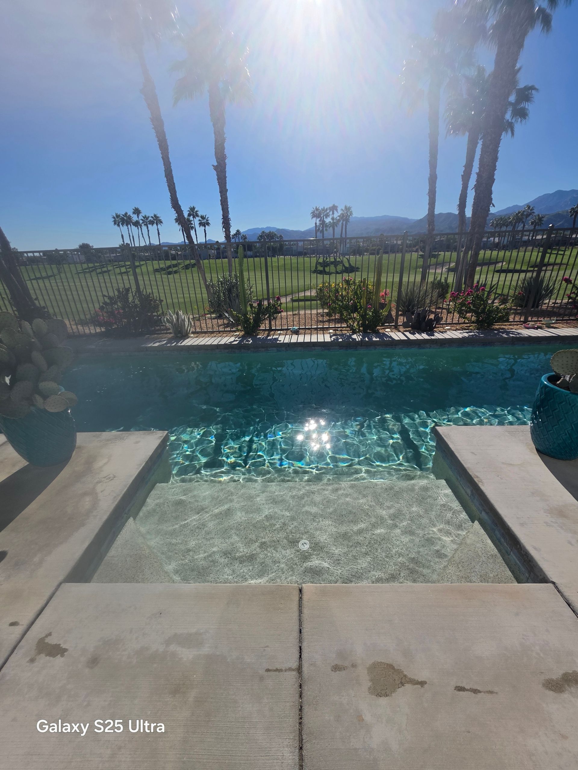 Swimming pool with steps, turquoise water, sunny day, palm trees and mountain backdrop.