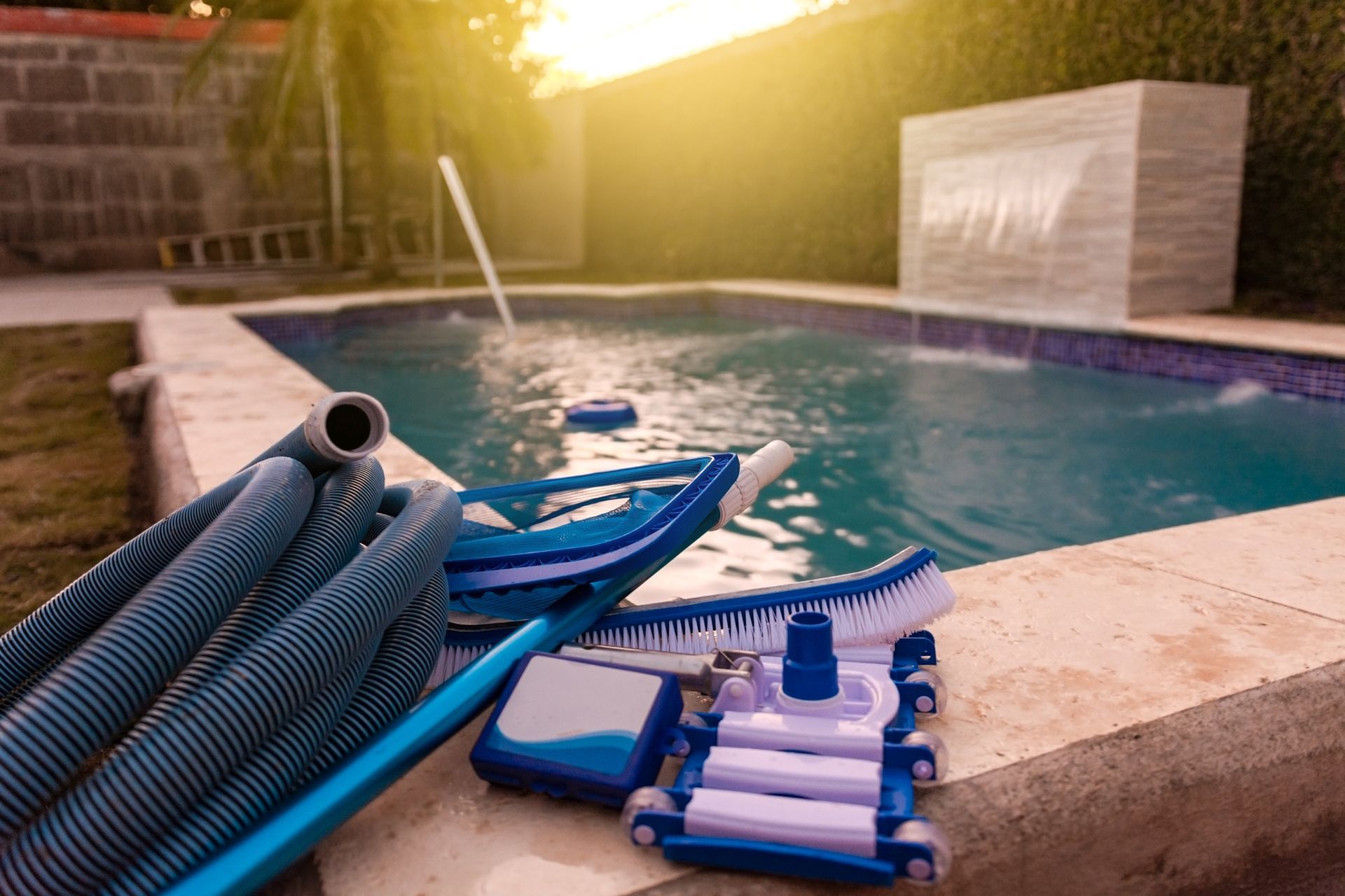 A hose , vacuum cleaner , and brush are sitting on the edge of a swimming pool.