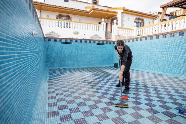 A man is cleaning the floor of an empty swimming pool with a mop.