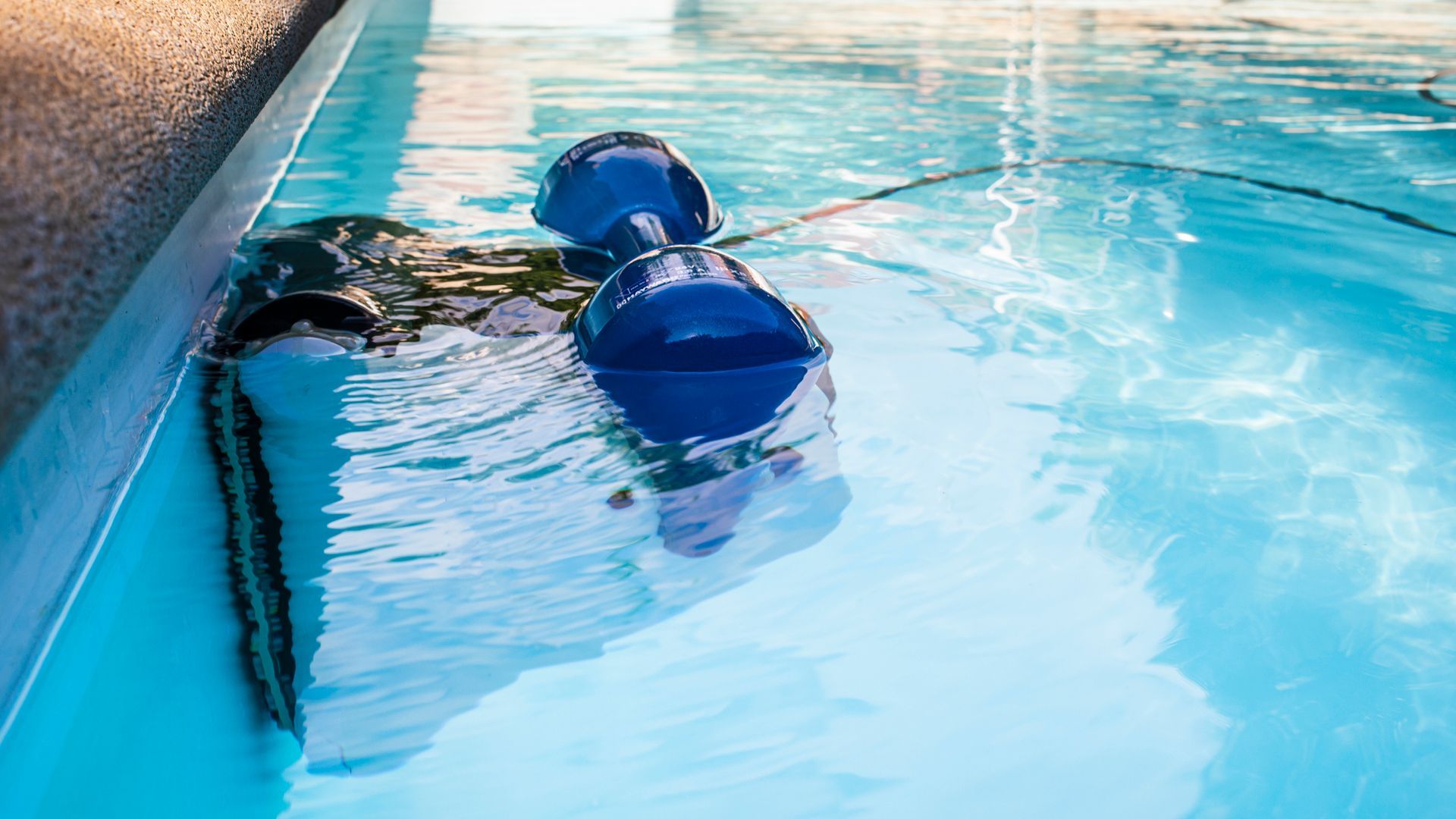 A person is swimming in a swimming pool with a robotic vacuum cleaner.