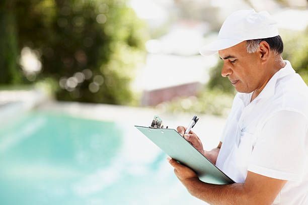 A man is looking at a clipboard in front of a pool.