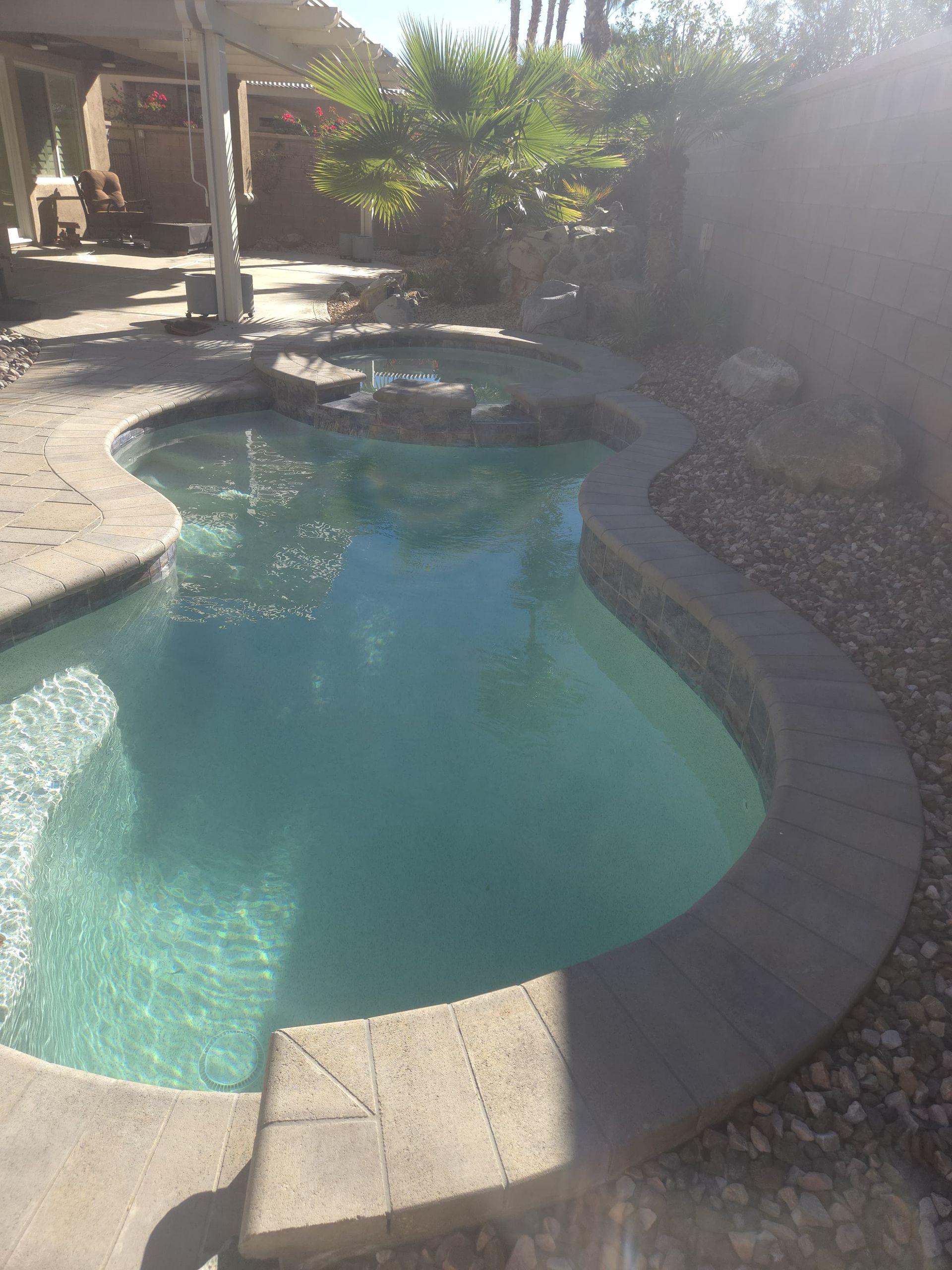Swimming pool with curved edges, built-in spa, surrounded by concrete and gravel landscaping.