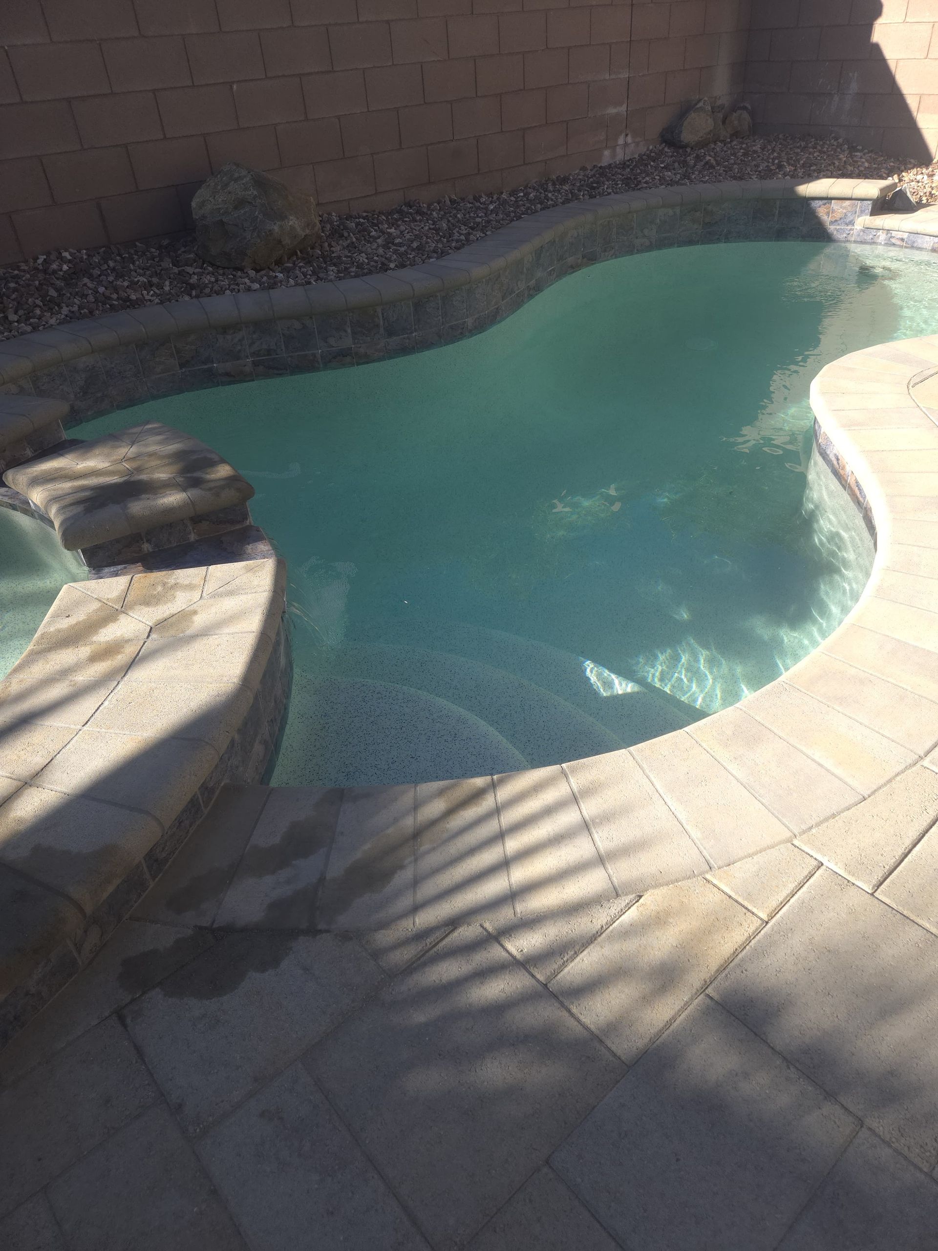 A kidney-shaped pool with light blue water and stone steps.