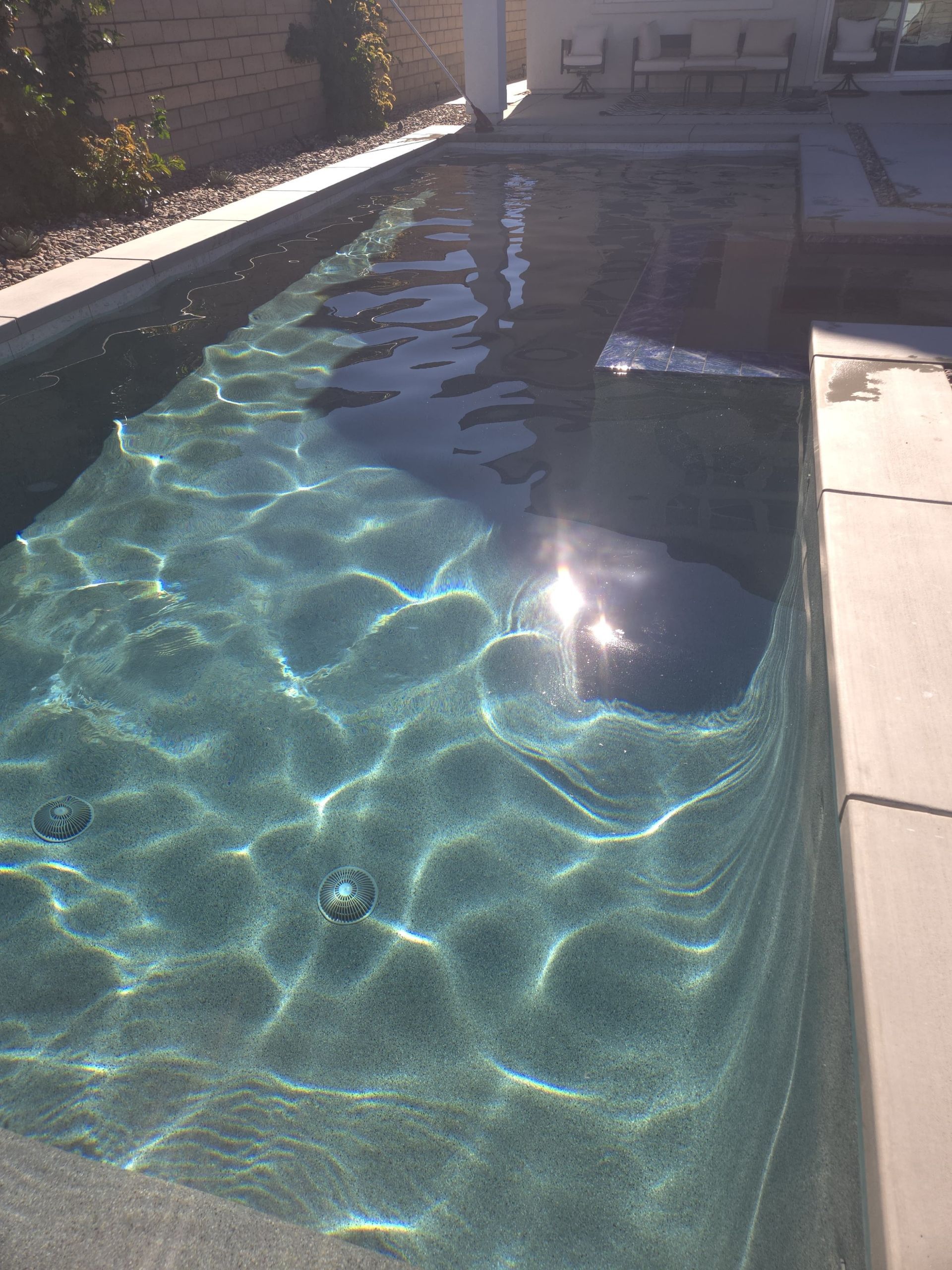 Rectangular swimming pool with turquoise water reflecting sunlight. Concrete surrounding the pool.