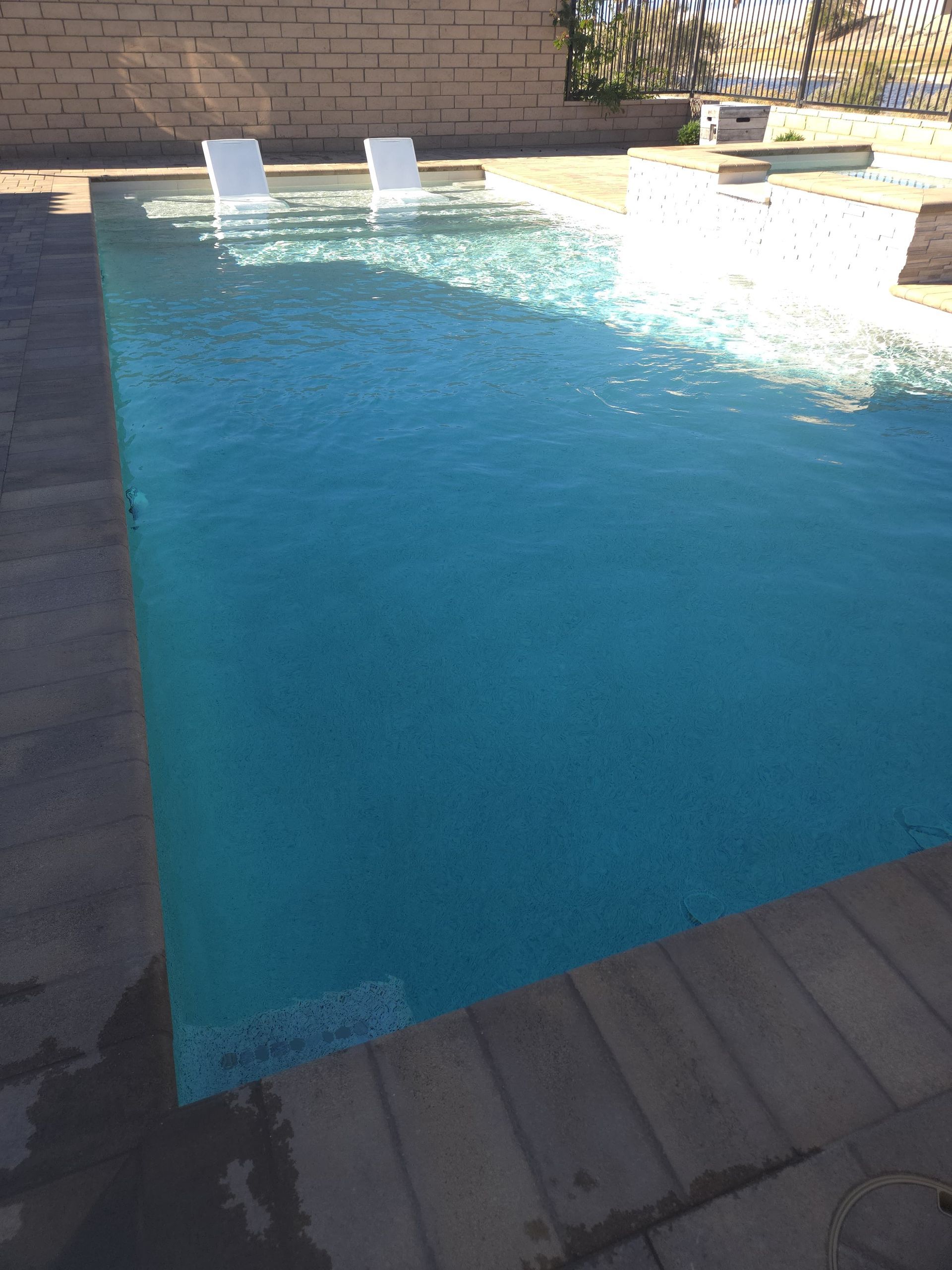 A rectangular swimming pool filled with turquoise water, surrounded by light-colored concrete.