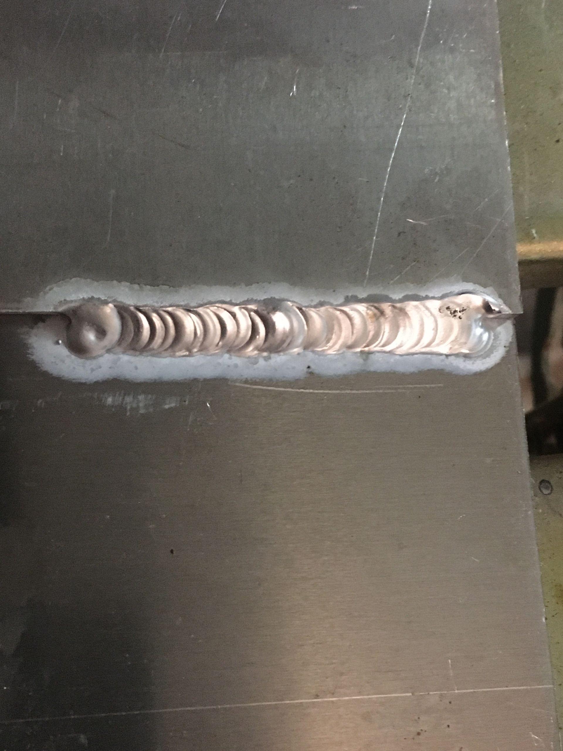 Metal sheets joined by a weld, silver-colored with rippled texture and some discoloration.