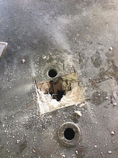 Close-up of a damaged metal surface with a large hole revealing the interior. Two smaller holes are visible.